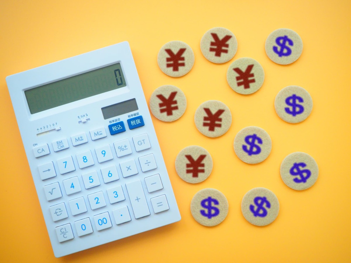 黄色の背景に白い計算機とたくさんの円やドルのマーク